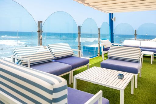 A cafe tables and chairs with blue and white strips with a great view of the sea