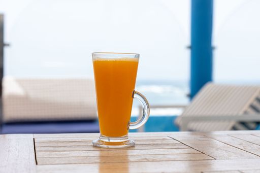 A closeup shot of a glass of orange juice on a table with a blue sky and the sea in its background