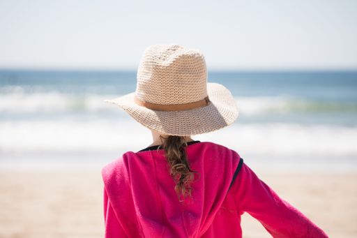 A back view of a girl wearing a straw hat and walking on the beach