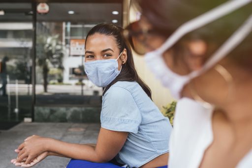 A young Hispanic girl with a medical mask talking to her friend and social distancing