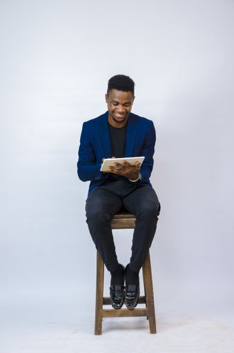 A young handsome African businessman sitting on a chair, holding a tablet and smiling