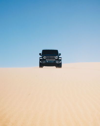 The vertical view of a black Jeep on the sand dune under the blue sky