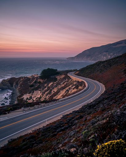 A vertical shot of Pacific coast highway surrounded by growing grass in California during sunset