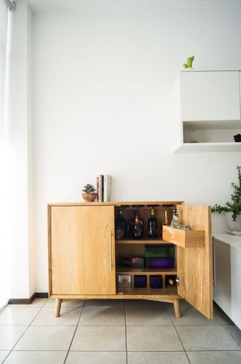 A vertical shot of a wooden alcohol cabinet in the room with the white wall on the background