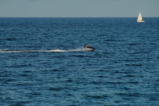 A man jet skiing in the blue sea with sailboat in the background
