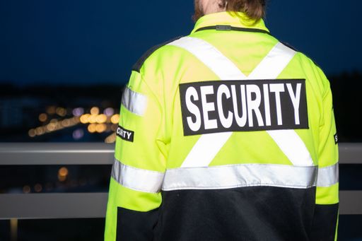 A closeup of a security guy in a bright green uniform standing near a handrail.