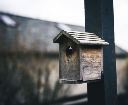 A closeup of a handmade wooden bird house hanging on a metallic post