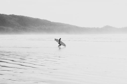 A grayscale shot of a lonely surfer entering the sea in Tofino, British Columbia, Canada