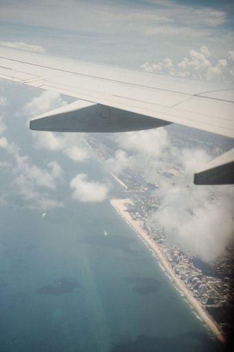A vertical shot of an airplane wing above the sea and clouds