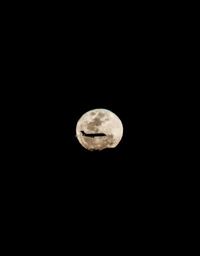 An airplane flying against full moon in night sky