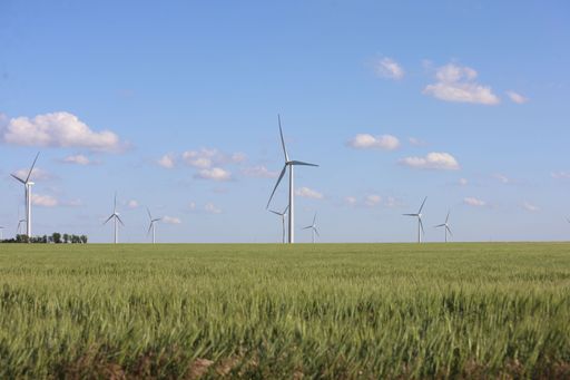 A landscape with wind generator turbines in a green field and a cloudy blue sky in the background