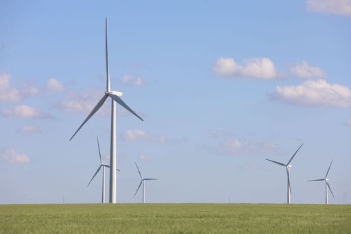 A landscape with wind generator turbines in a green field and a cloudy blue sky in the background