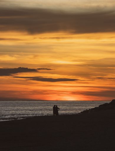 A vertical shot of a couple standing on the beach at sunset with a cloudy sky in the background, Puerto Vallarta, Mexico