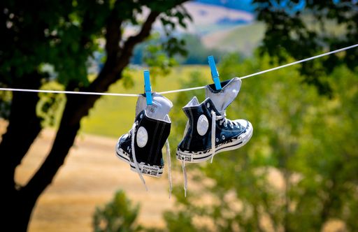 A closeup shot of black and white Converse All Stars trainers, drying on a clothesline, and countryside with trees and wheat fields in the background