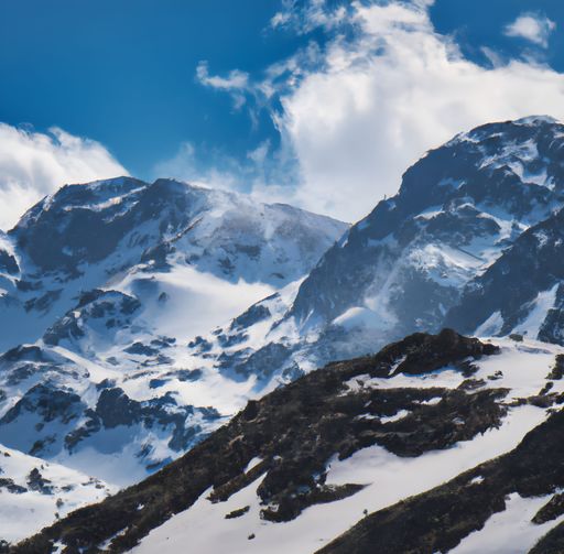 A landscape of rocky mountains covered in the snow under the sunlight and a blue cloudy sky