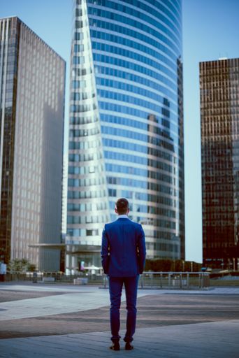 A young businessman standing on a high glass building background, view from the back