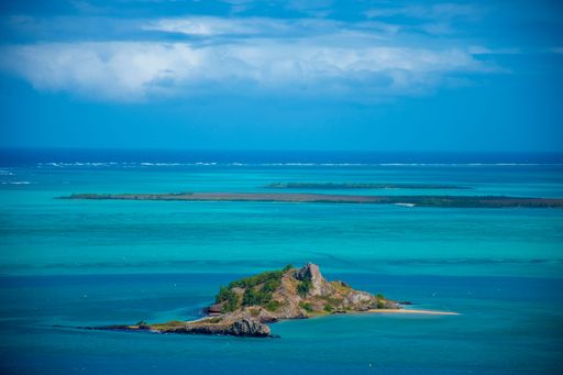The aerial view of a small island in the blue ocean under the blue cloudy sky