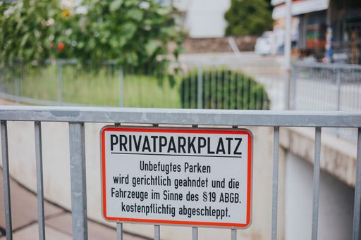 A closeup of a sign of "private parking place" in German on metallic bars