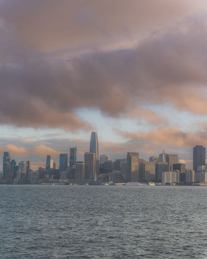 The vertical view of the San Francisco city buildings by the sea under the cloudy sky at sunset