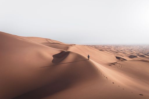 A man walking on the sand dunes alone in desert landscape under the bright sky