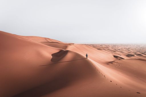A man walking on the sand dunes alone in desert landscape under the bright sky