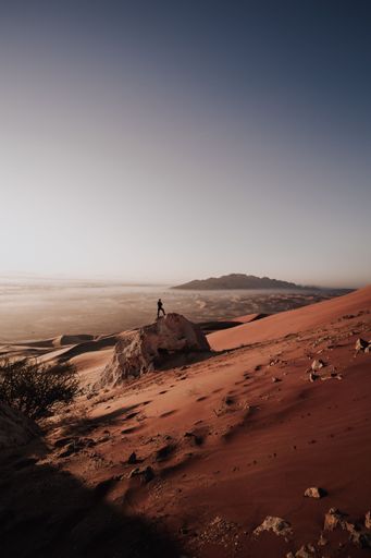 The vertical view of a man standing on the rock alone in sand dunes of desert under the bright sky