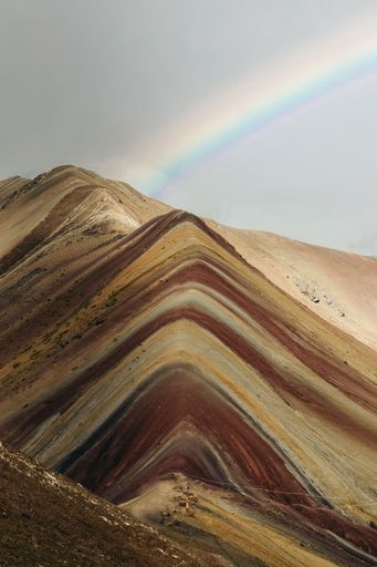 A vertical shot of the Rainbow Mountain in Peru with a rainbow in the sky