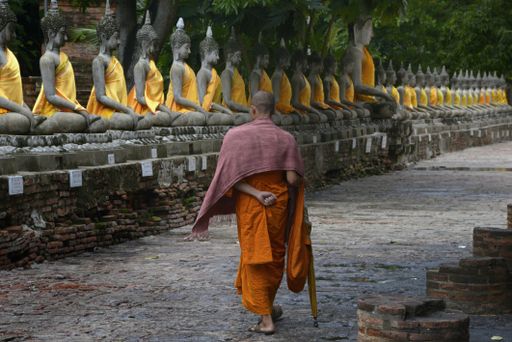 An eye-level shot of a monk walking around the statues of Buddha in Wat Yai Chaimongkol temple in Ayutthaya, Thailand