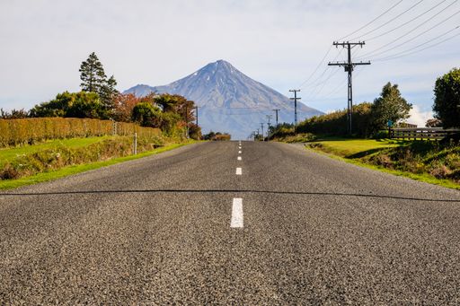 A scenic view of an open road surrounded by greenery with Taranaki mountain in the background