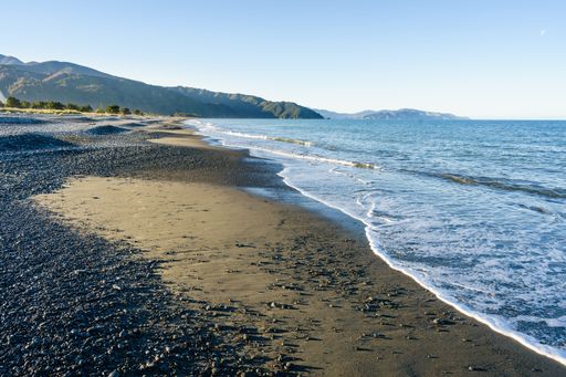 The beautiful sandy and rocky Rarangi beach in New Zealand with the ocean and sunlight reflected in the foamy waves, with a mountain in the background