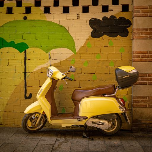 Bright yellow moped against a colourful brick wall