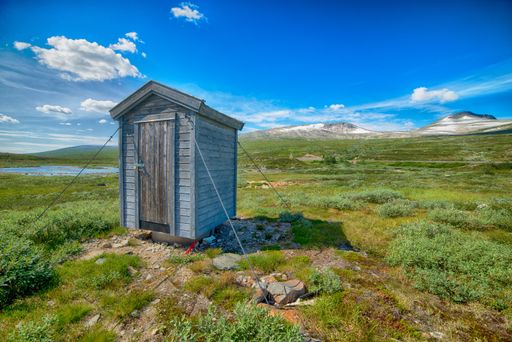 A beautiful shot of a wooden portable bathroom in the center of a green field with the sky in the background