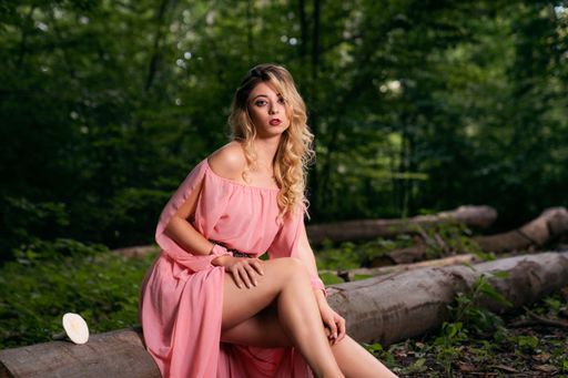 A pretty caucasian blonde woman in a short pink dress sitting on falling log tree in the park