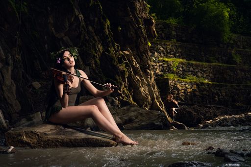 A Pretty caucasian girl in brown short dress with a flowers crown sitting on a rock in the park river
