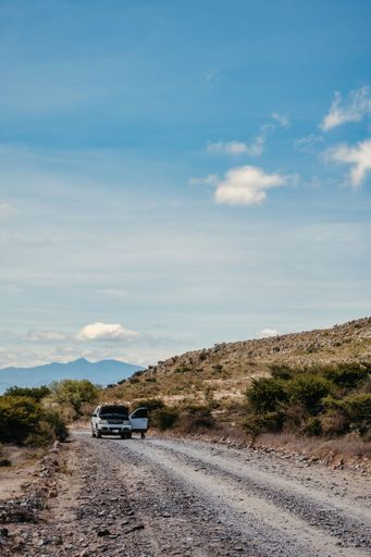 A vertical shot of an off-road broken car on a rocky highway road with a cloudy blue sky in the background