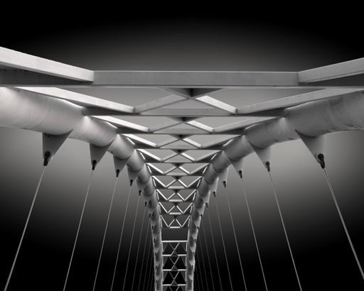 A gray scale closeup shot of a metal bridge with wires connected to it