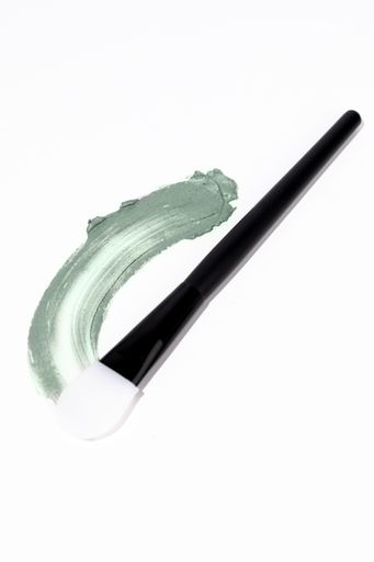 Minimal White Background Photo of Black and White Silicon Face Mask Application Brush With a Natural Fresh Green Face Mask Treatment Swatch