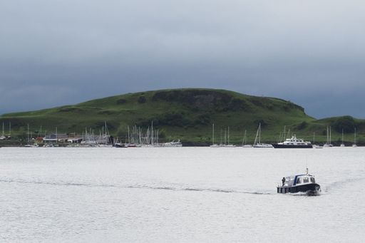 The view of the green hill with moored boats near the shore.
