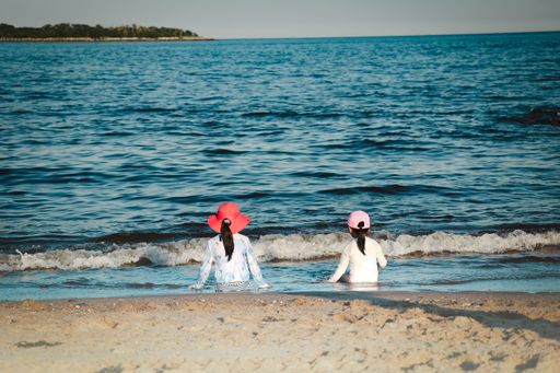 A beautiful view of two little girls sitting by the wavy beach and looking at the horizon