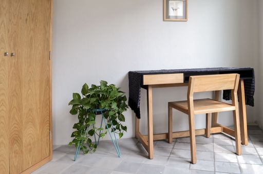 A wooden desk with a chair, plants, pasta tile floor, and white walls in a cozy contemporary design