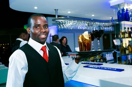 An African male waiter holding a tray of drinks in a bar in Johannesburg, South Africa