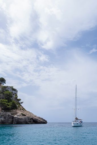 a sailboat anchored at the entrance of a cove, near a cliff , cala Galdana, Menorca, Balearic Isalas, Spain, vertical