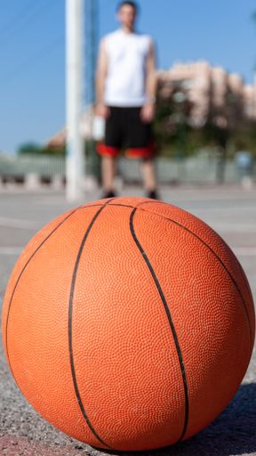 A vertical selective focus shot of a basketball ball in a court and a person in the background