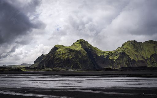 An amazing view of green mountains and black sand under a cloudy sky