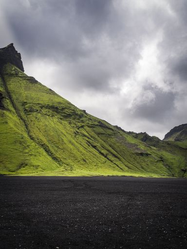 An amazing view of green mountains and black sand under a cloudy sky