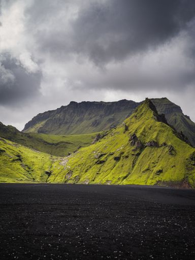 An amazing view of green mountains and black sand under a cloudy sky