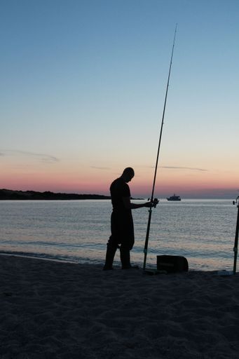 A silhouette of a man near the beach with his head down and fishing gear in his hand