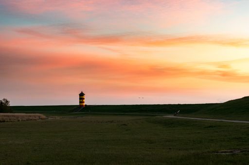 A lighthouse in a green field by the sea during sunset