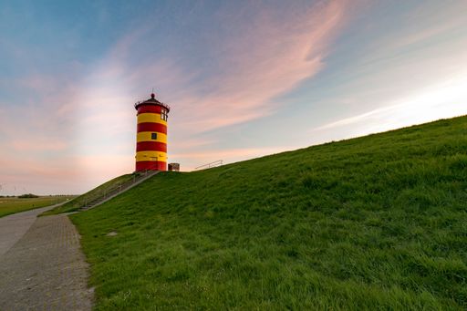 A lighthouse in a green field by the sea during sunset