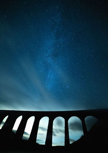 A vertical shot of the blue starry sky at night over a viaduct